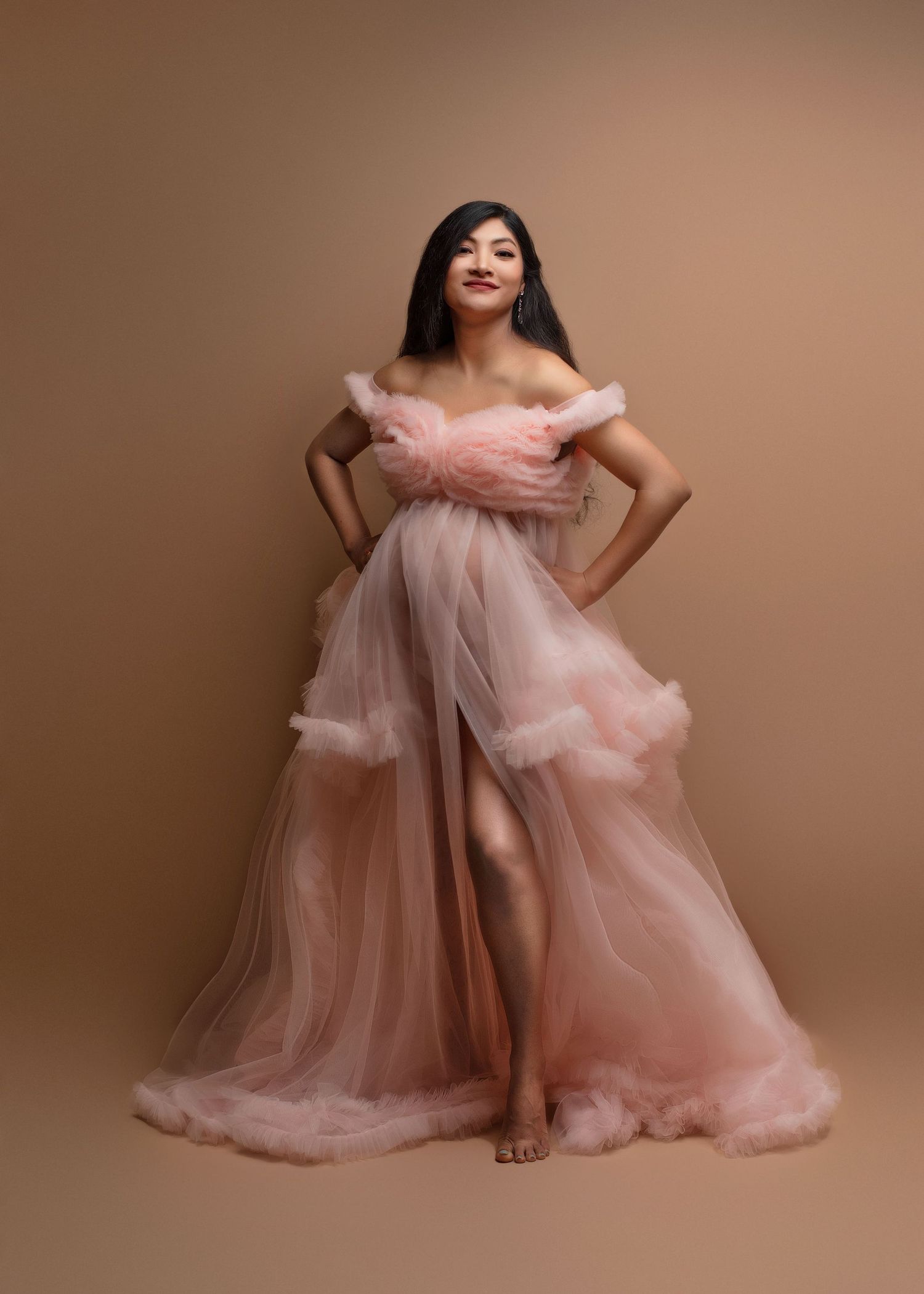 a woman smiles with her hands on her hips while wearing a fluffy pink dress
