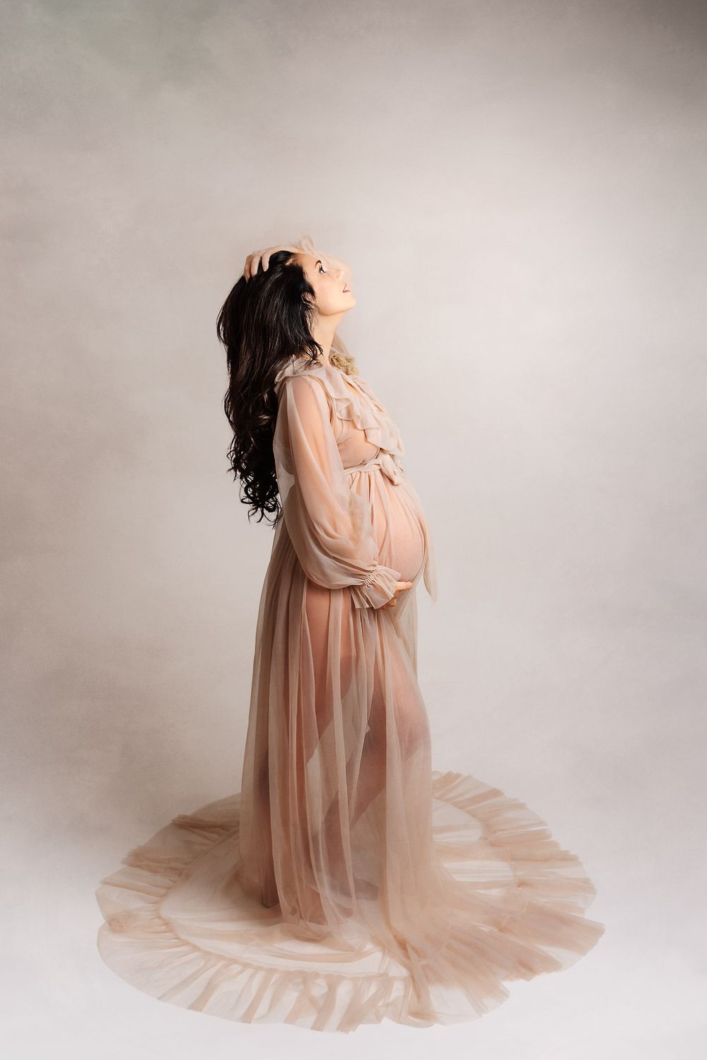 Artistic maternity portraits showing a woman in a flowing peach gown against a neutral studio backdrop.