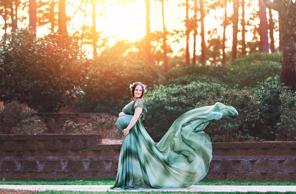 Flowing green dress catches sunlight in a forest setting during golden hour.