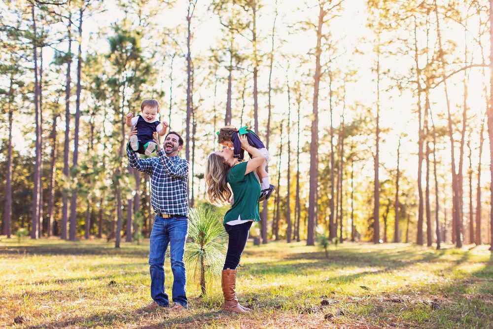 Family enjoying a playful moment in pine forest bathed in warm evening light.