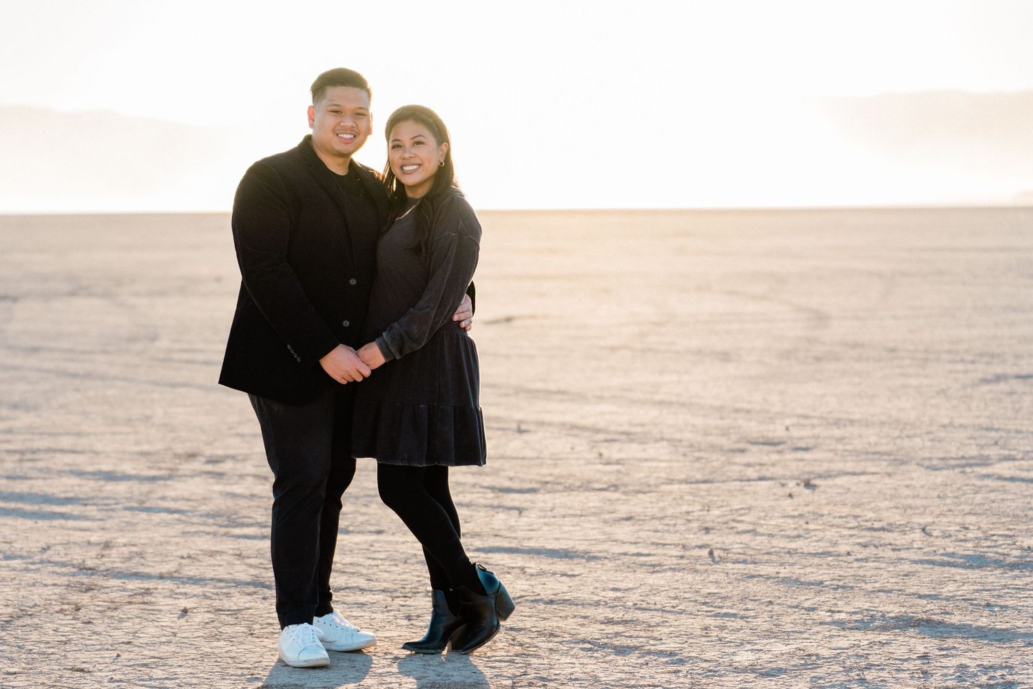 A couple in black coats poses together on a frozen winter landscape.