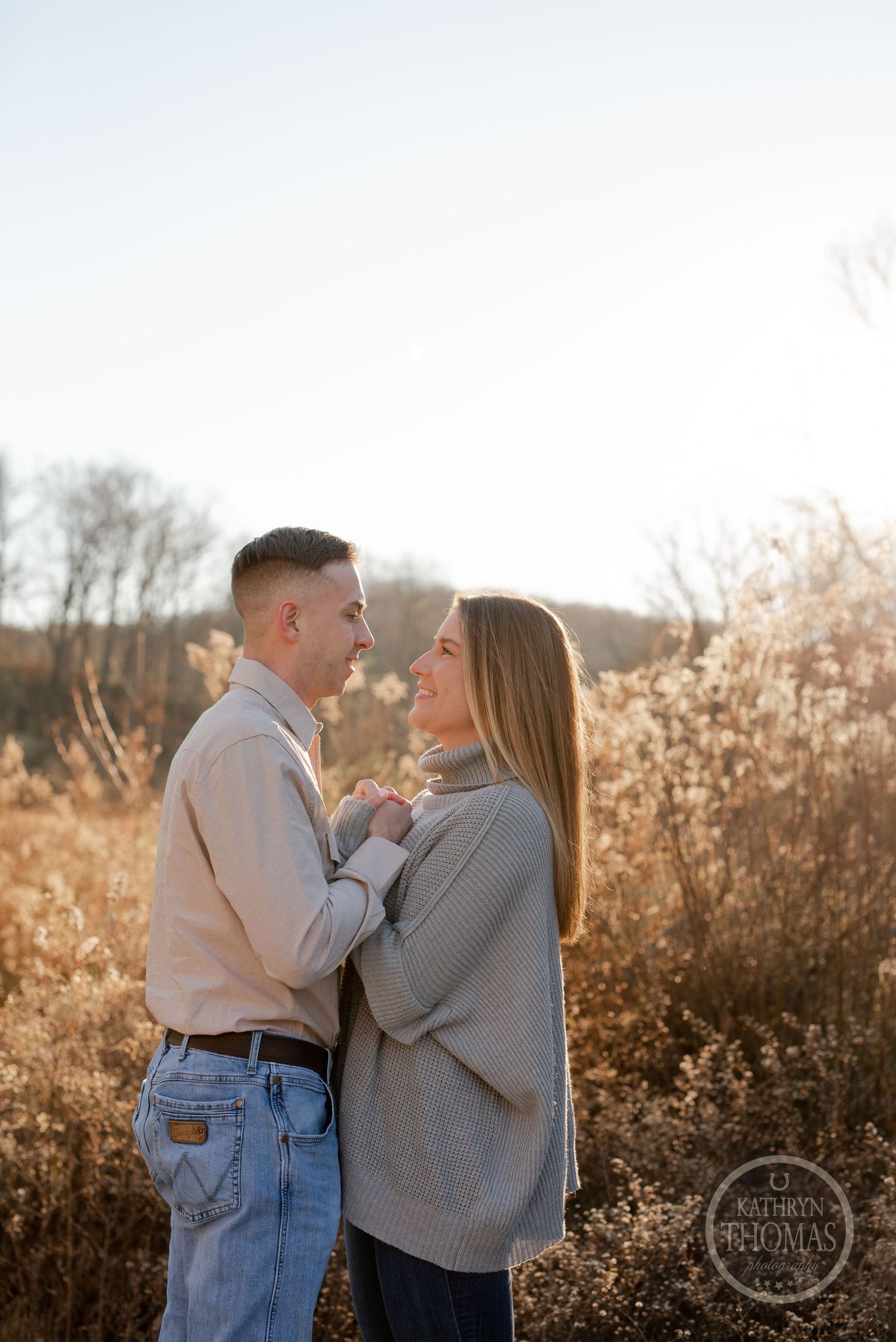 A couple sharing an intimate moment in a field during golden hour as sunlight filters through autumn foliage.