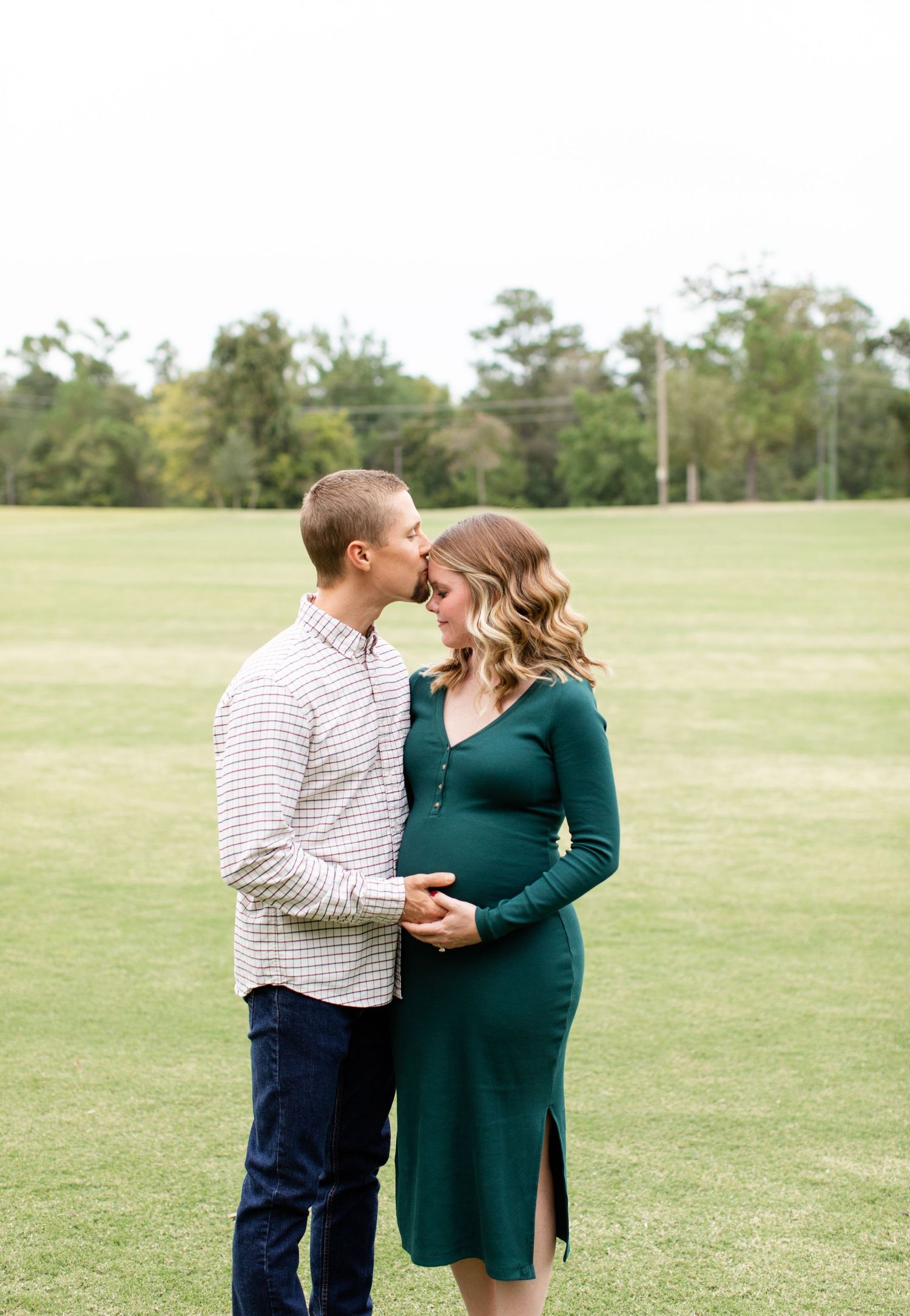 Sweet maternity moment captured in an open field with couple in matching white and green outfits.