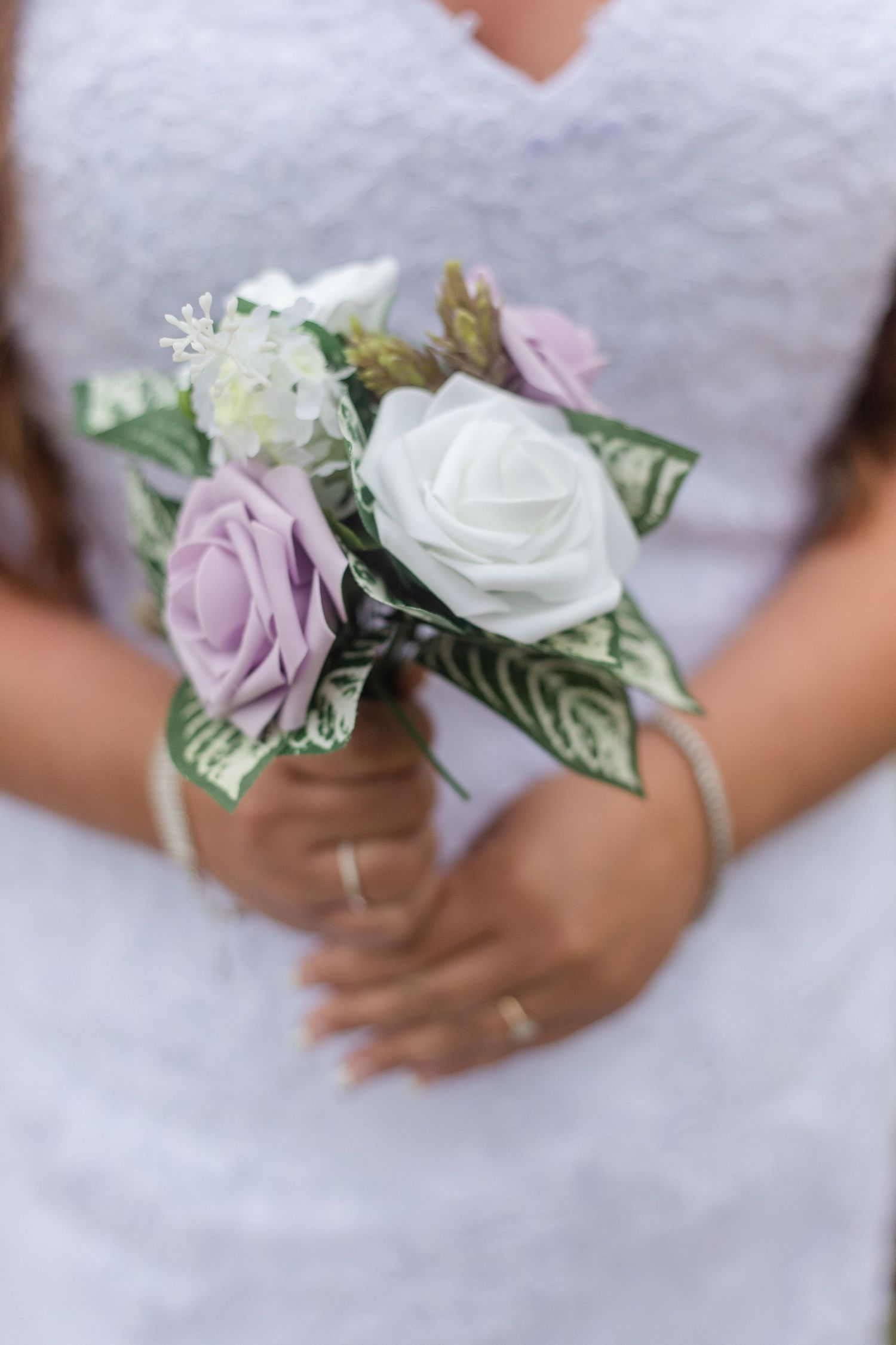 Close-up of delicate white and lavender rose bouquets against a white lace dress.
