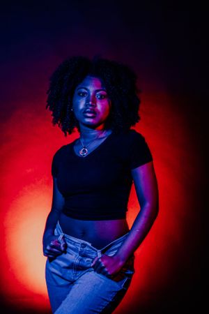 Dramatic portrait in blue and red lighting featuring a model in black top and jeans creating artistic poses against dark background.