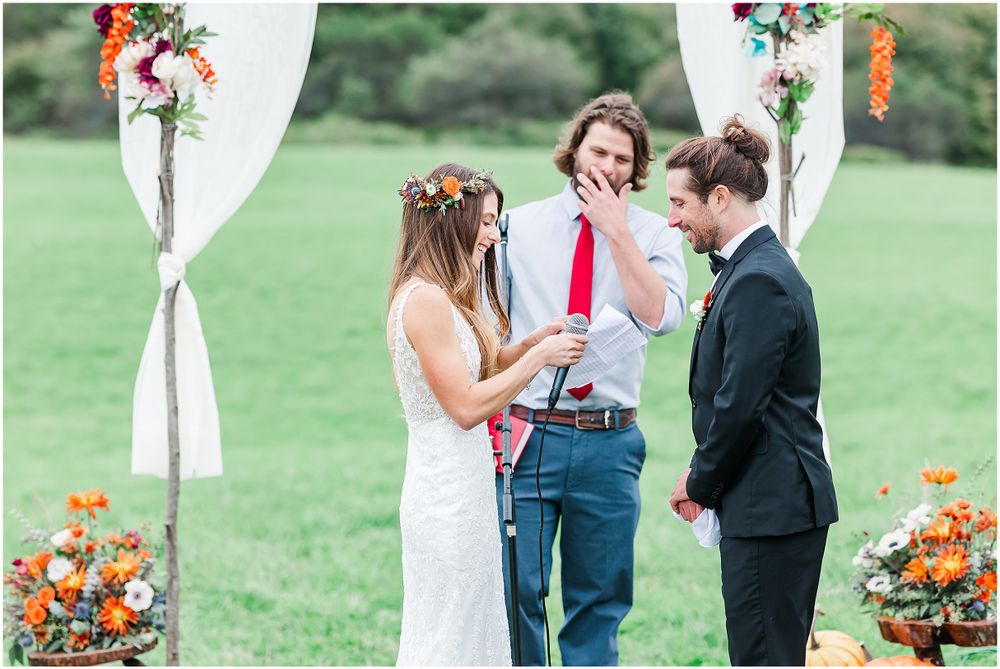 An outdoor wedding ceremony under white fabric archway decorated with orange flowers and greenery.