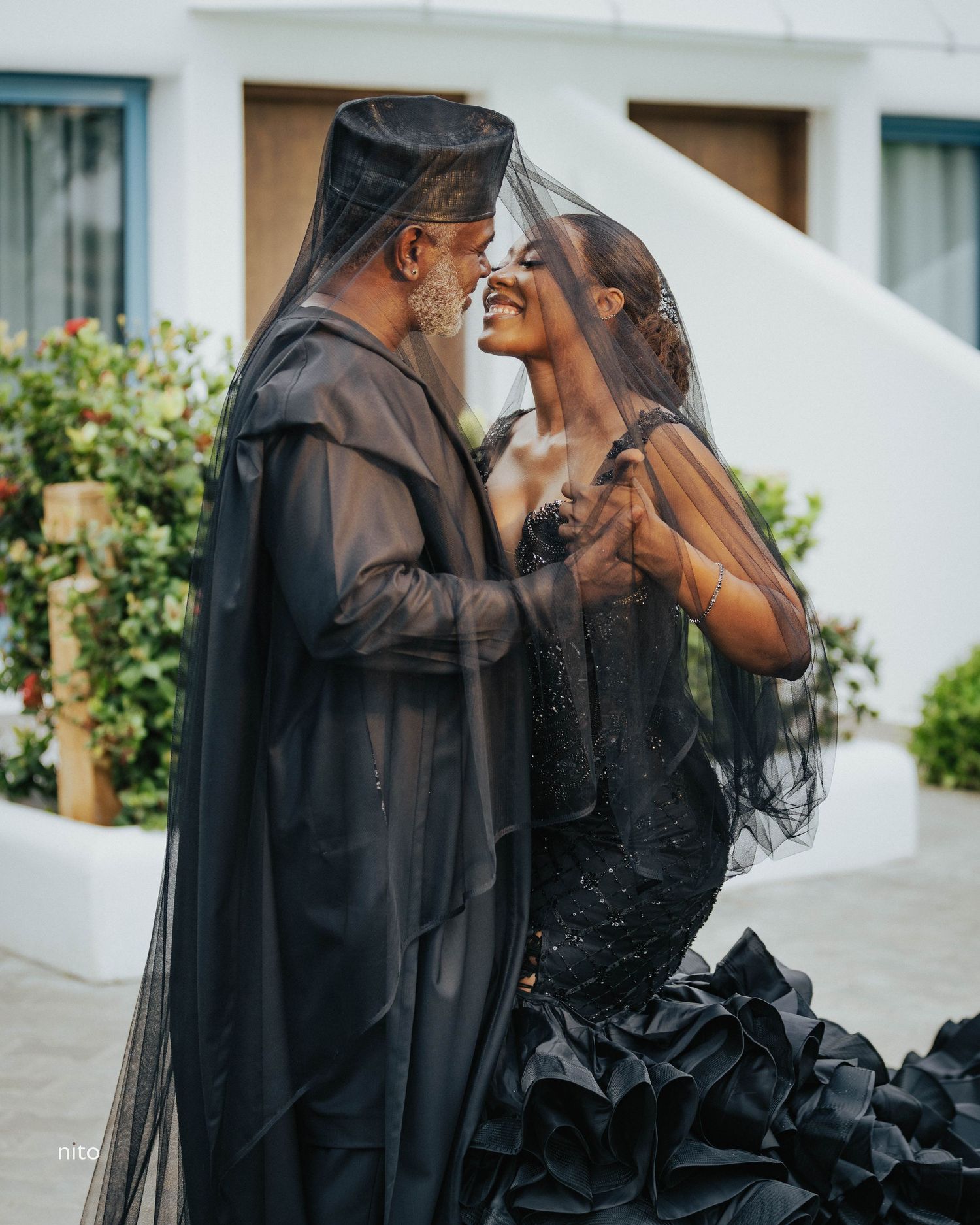 Couple sharing a romantic moment in black wedding attire with dramatic veils.