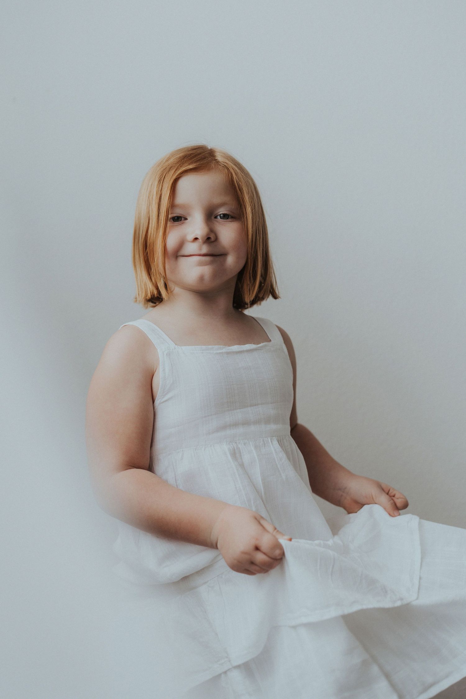 A redhead girl stands against a white paper backdrop