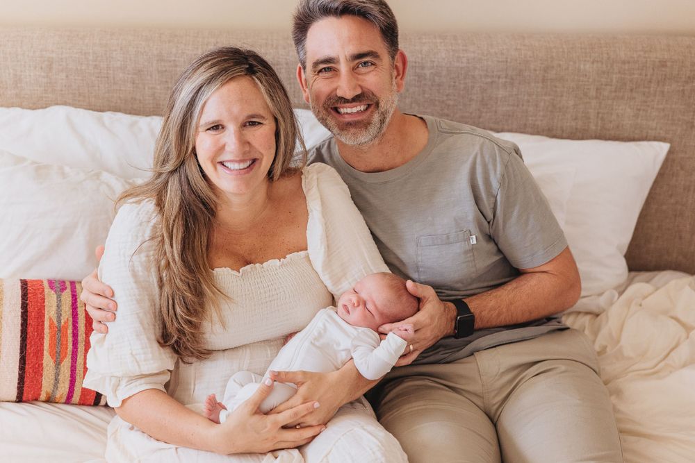 Happy couple sitting on bed with their newborn baby.