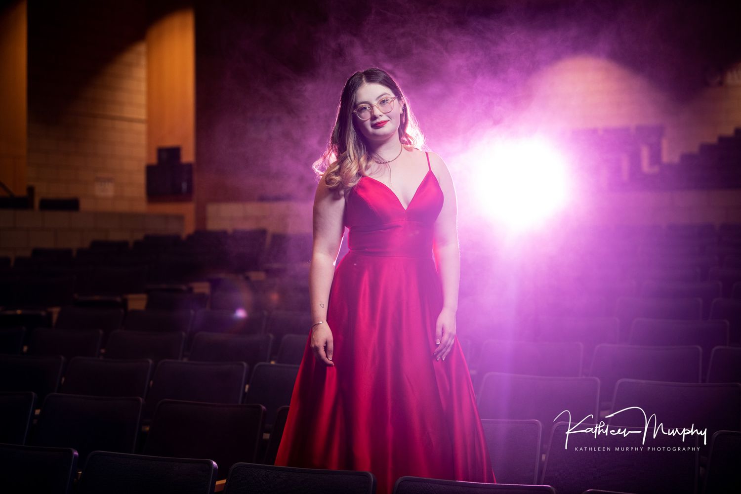 Dramatic portrait with red gown in theatrical lighting with purple backdrop.