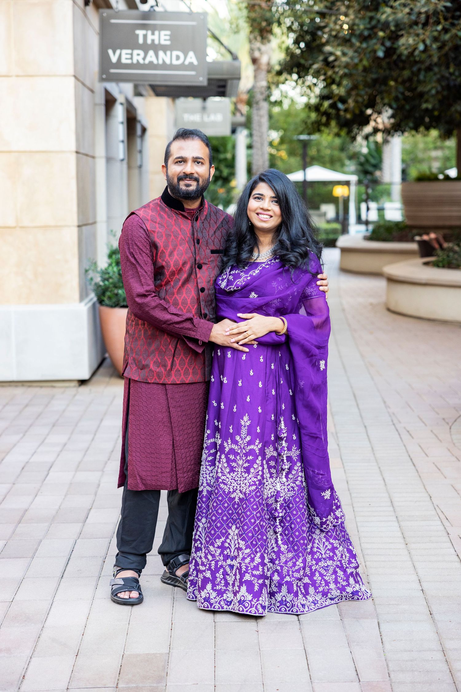 Couple in traditional Indian attire posing together outdoors near The Veranda sign.