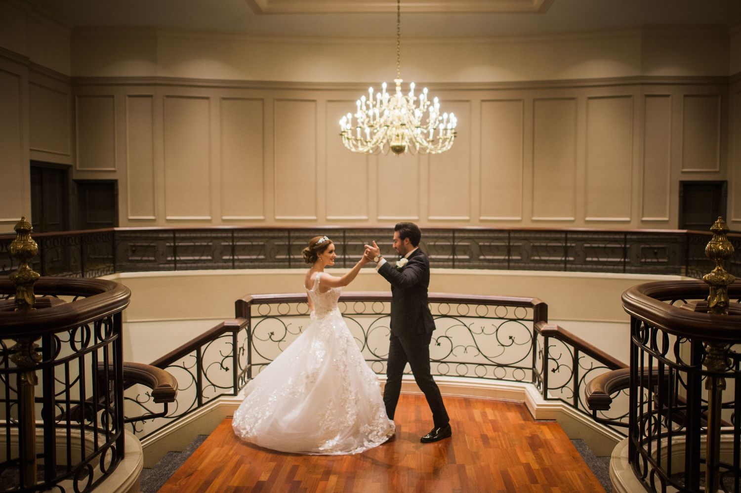 A romantic dance moment in an elegant ballroom with crystal chandelier and ornate railings.