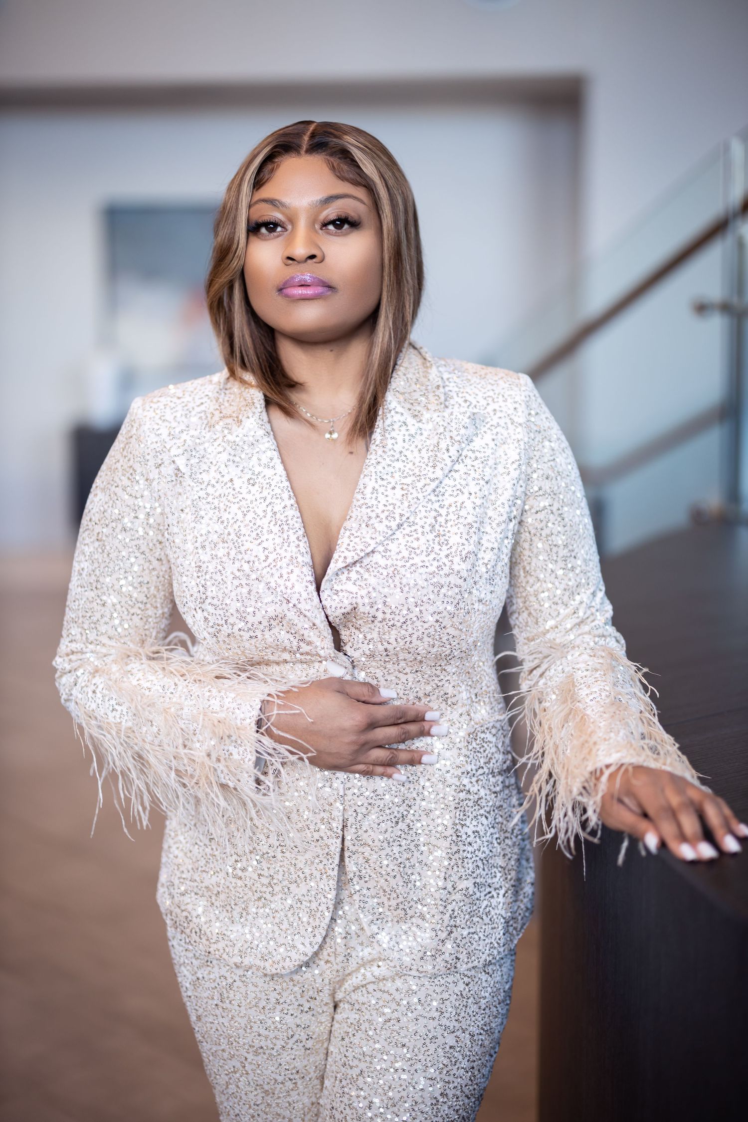 Person wearing glamorous white sequined suit with feather details poses on staircase.