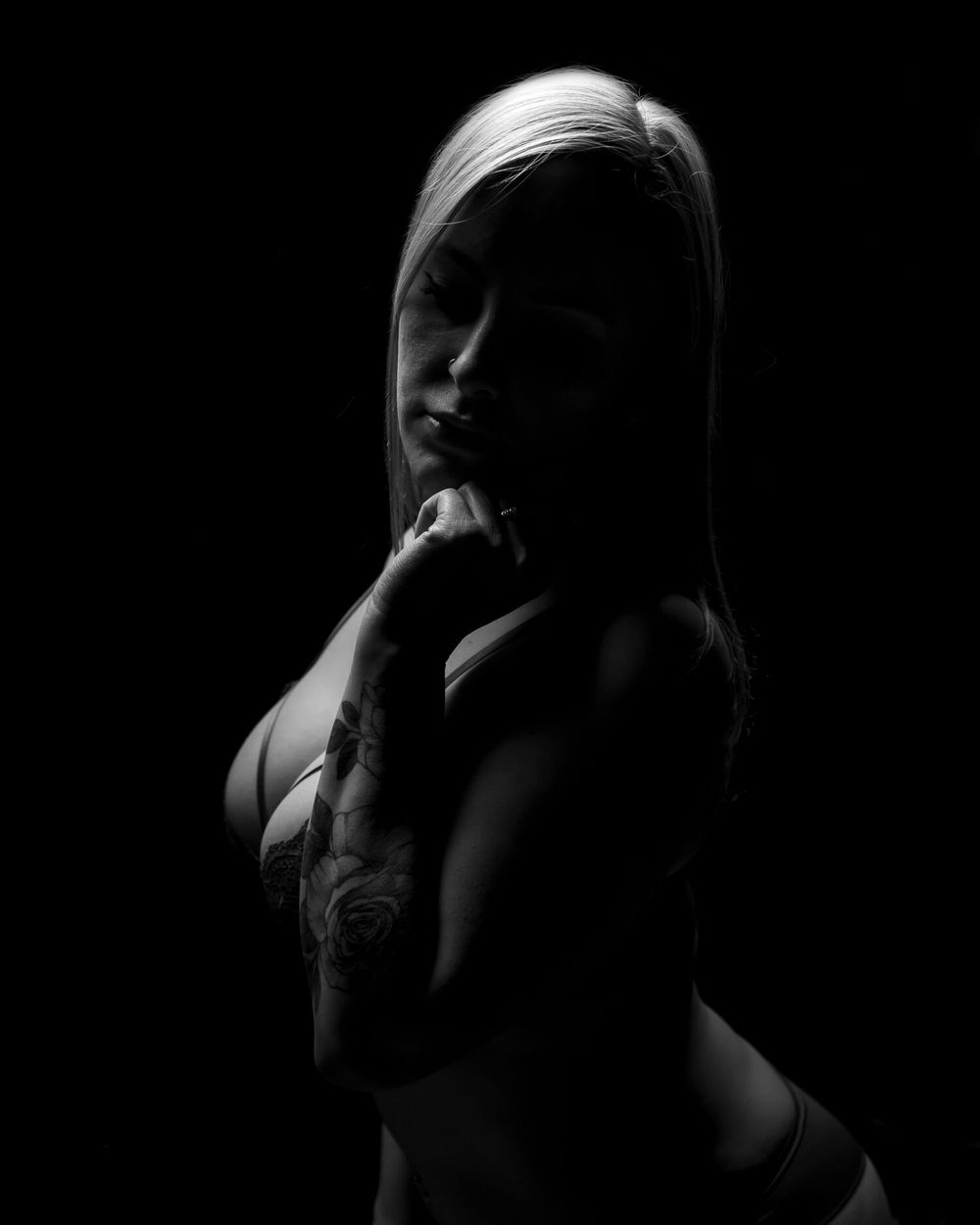 Artistic low key portrait photograph with dramatic shadows highlighting feminine silhouette against dark background.