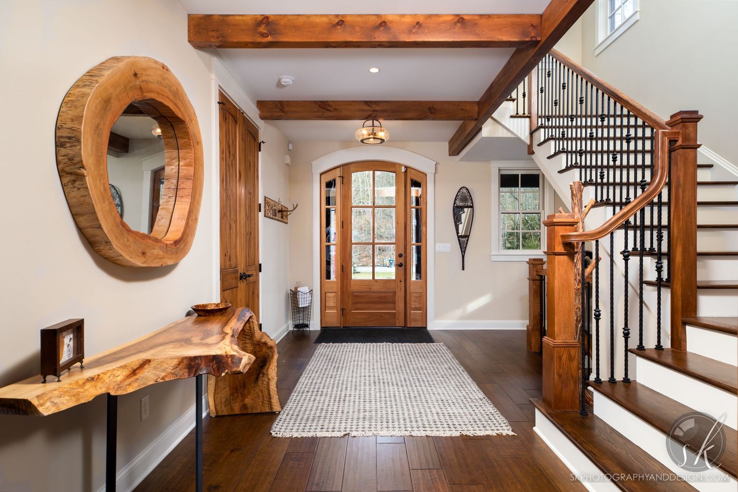 Modern rustic entryway with live edge wood console, round mirror, and wooden staircase.