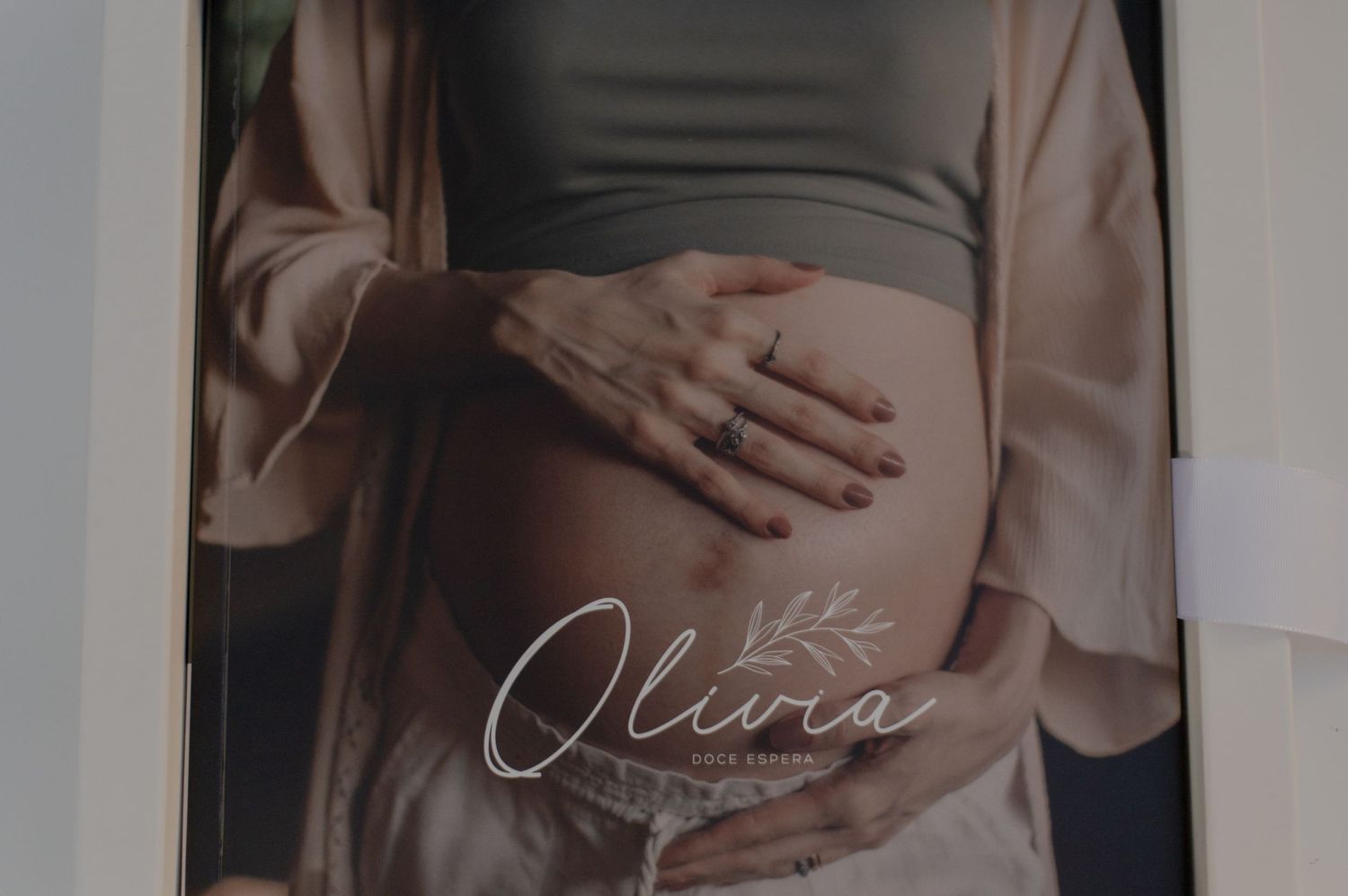 A maternity photo showing hands gently cradling a pregnant belly with the name Olivia overlaid in script text.