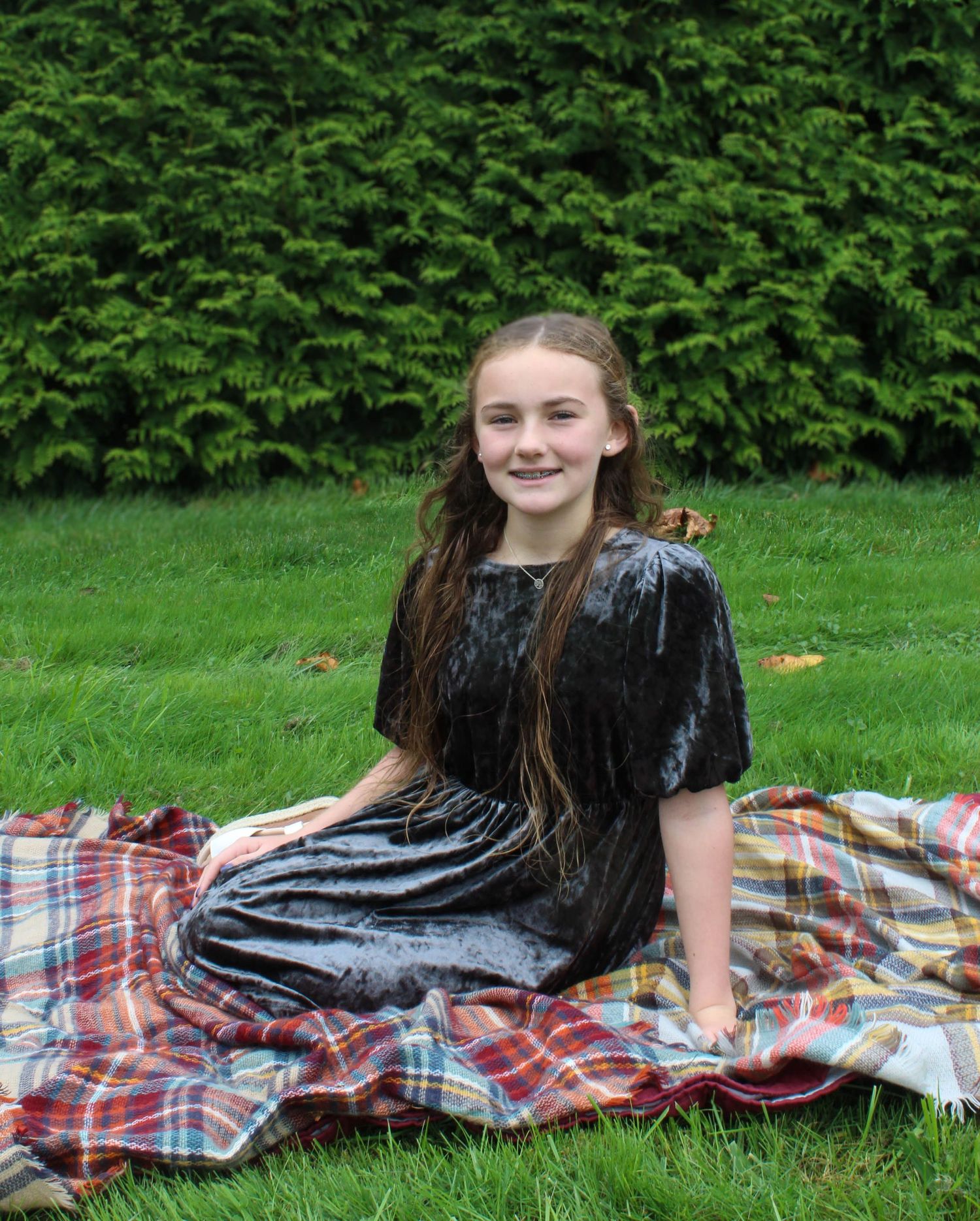 Person in a black velvet dress sitting on a plaid blanket outdoors.