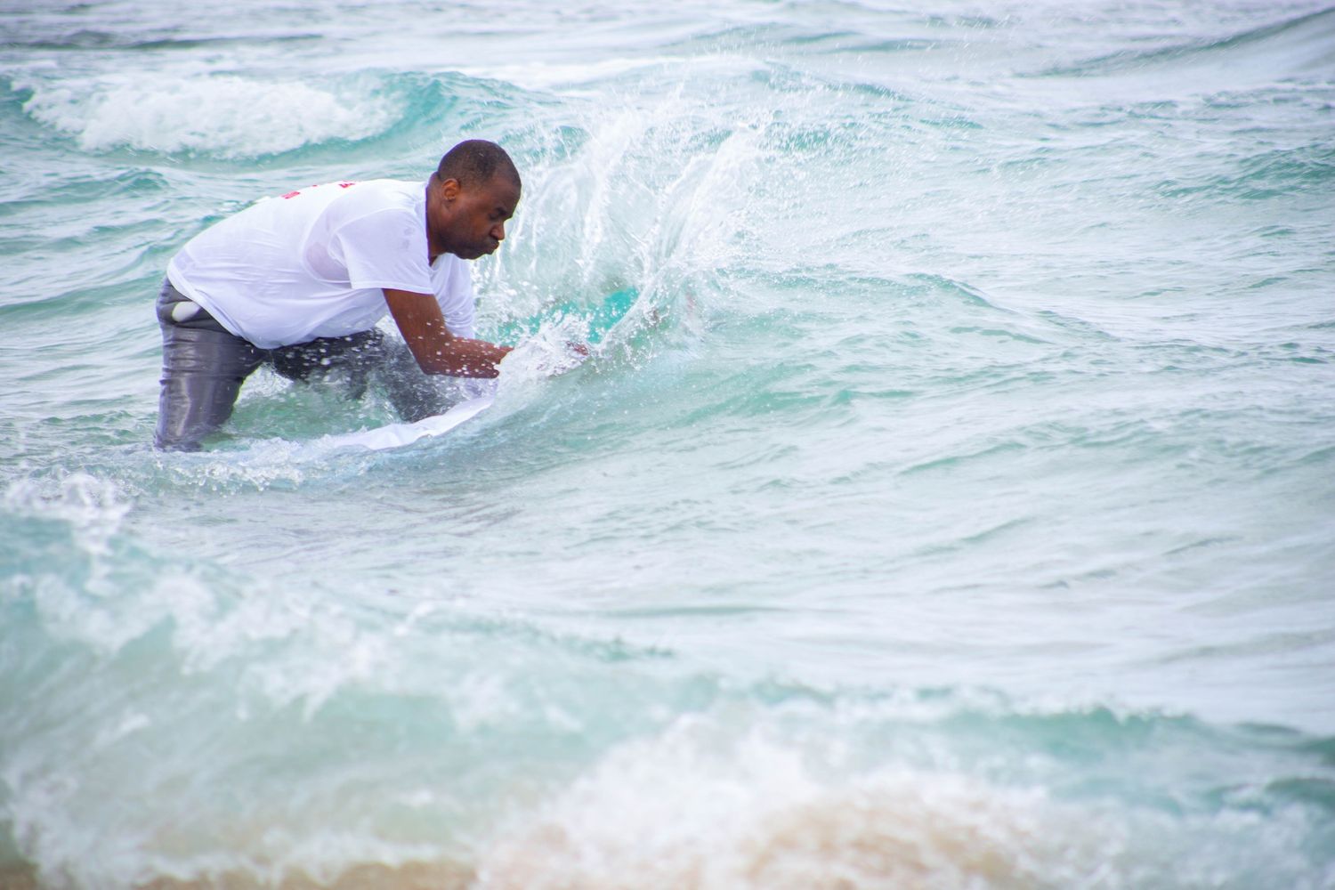 Person in white shirt splashing through ocean waves during beach photography session.