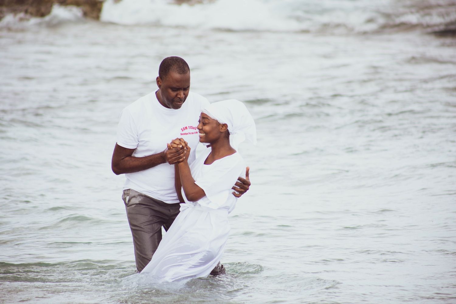 Couple in white and gray clothing sharing a romantic moment in the ocean waves.
