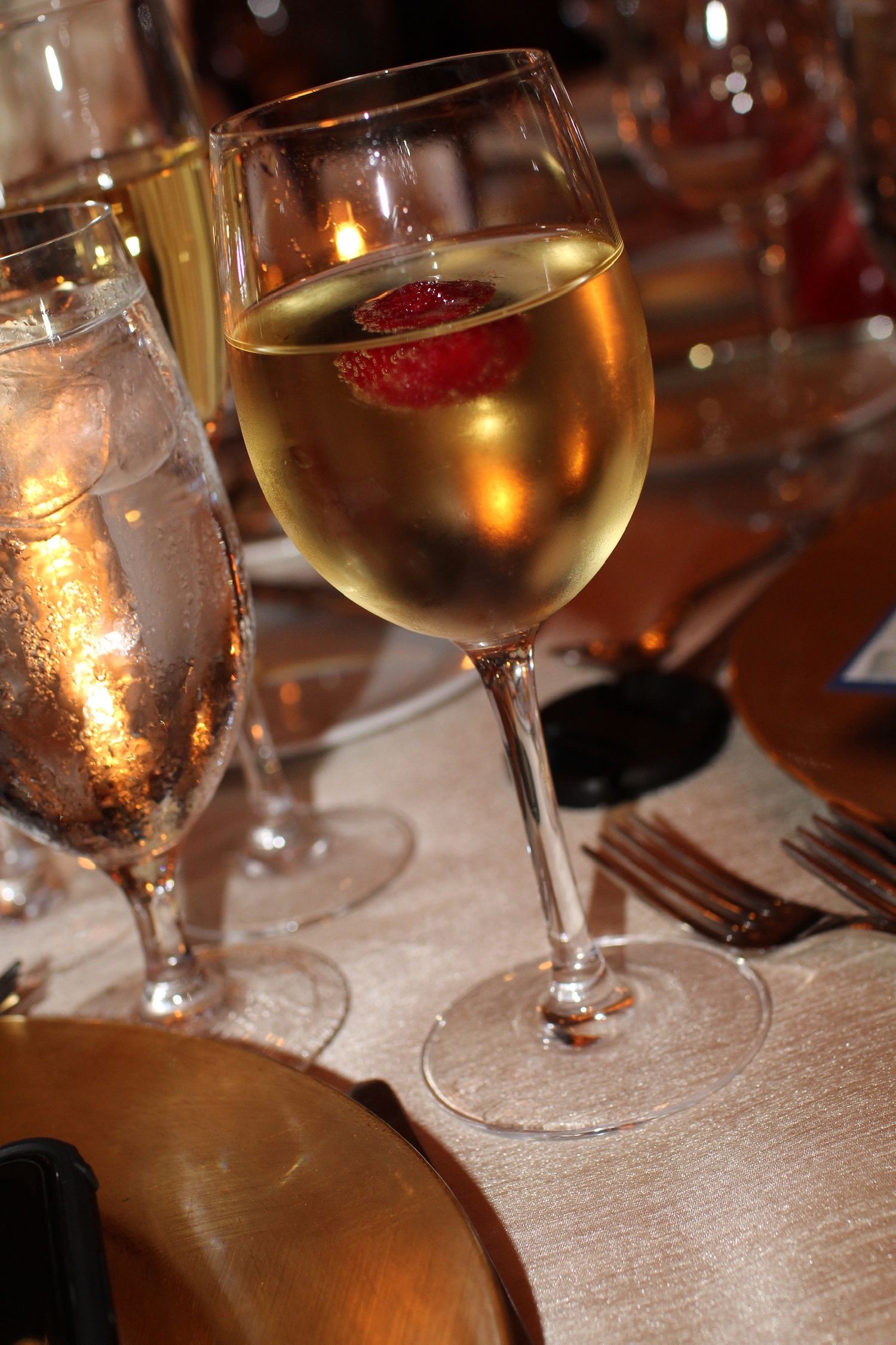 A glass of white wine with a strawberry garnish in elegant restaurant lighting.
