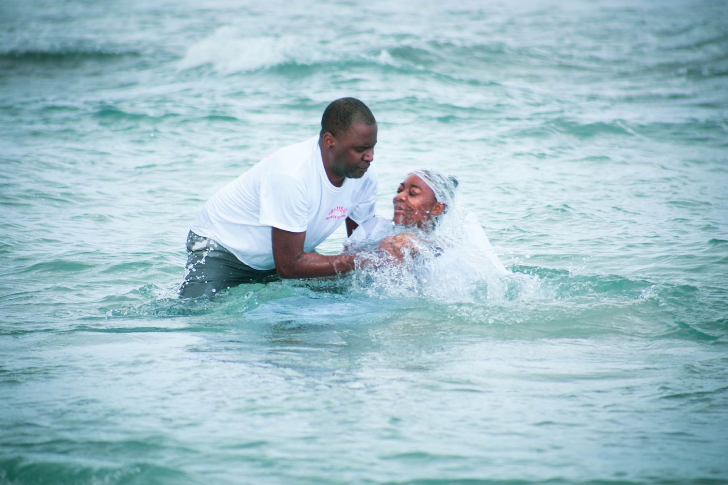 Baptism ceremony taking place in turquoise ocean waters with white clothing.
