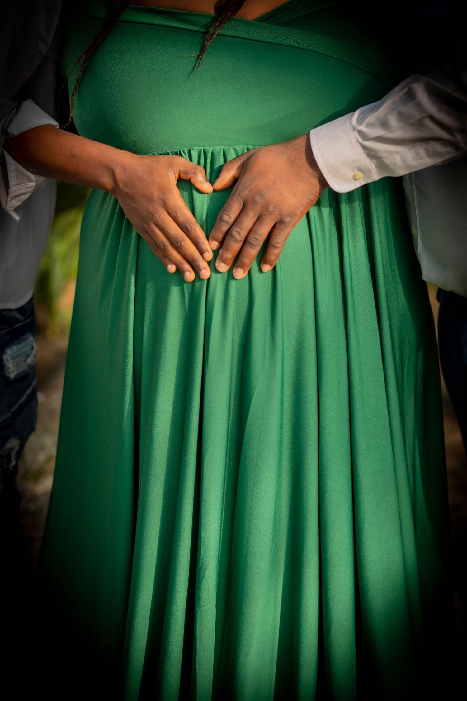 Hands forming a heart shape against a flowing emerald green dress in an intimate maternity photo.