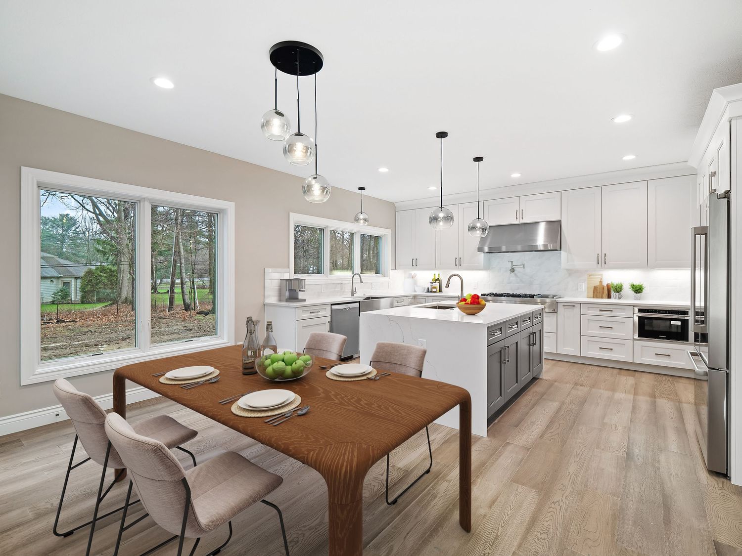 Modern open concept kitchen and dining area with white cabinets, wood floors and large windows overlooking nature.