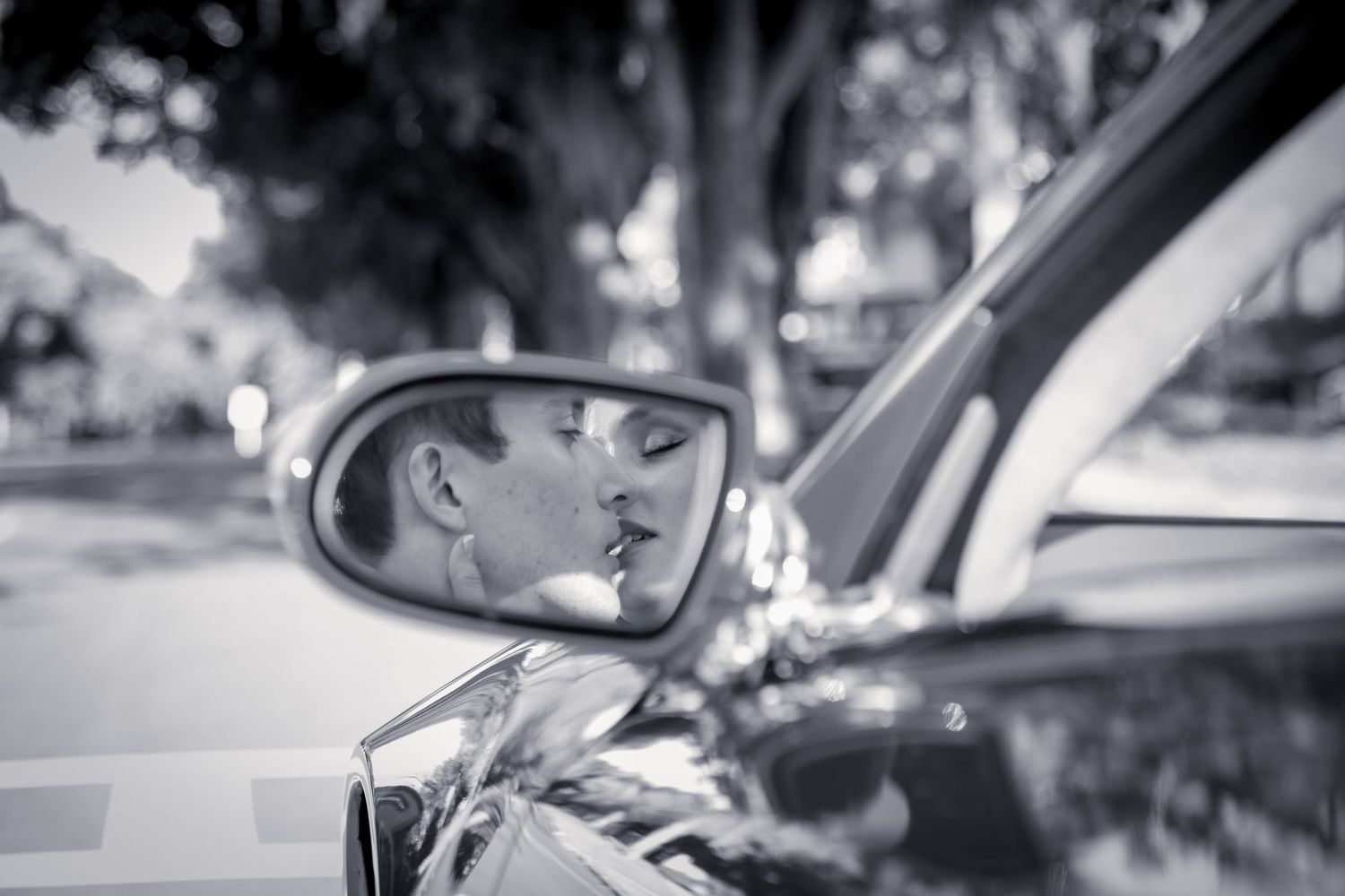 Artistic black and white reflection of a romantic moment captured in a car side mirror.