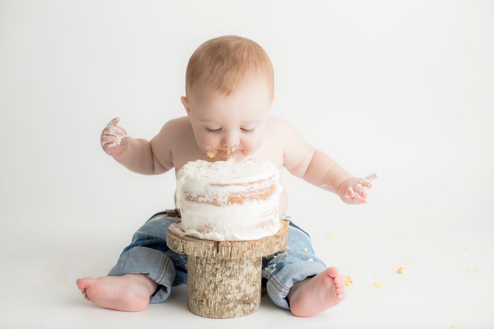 One year old baby boy eating cake with his mouth.