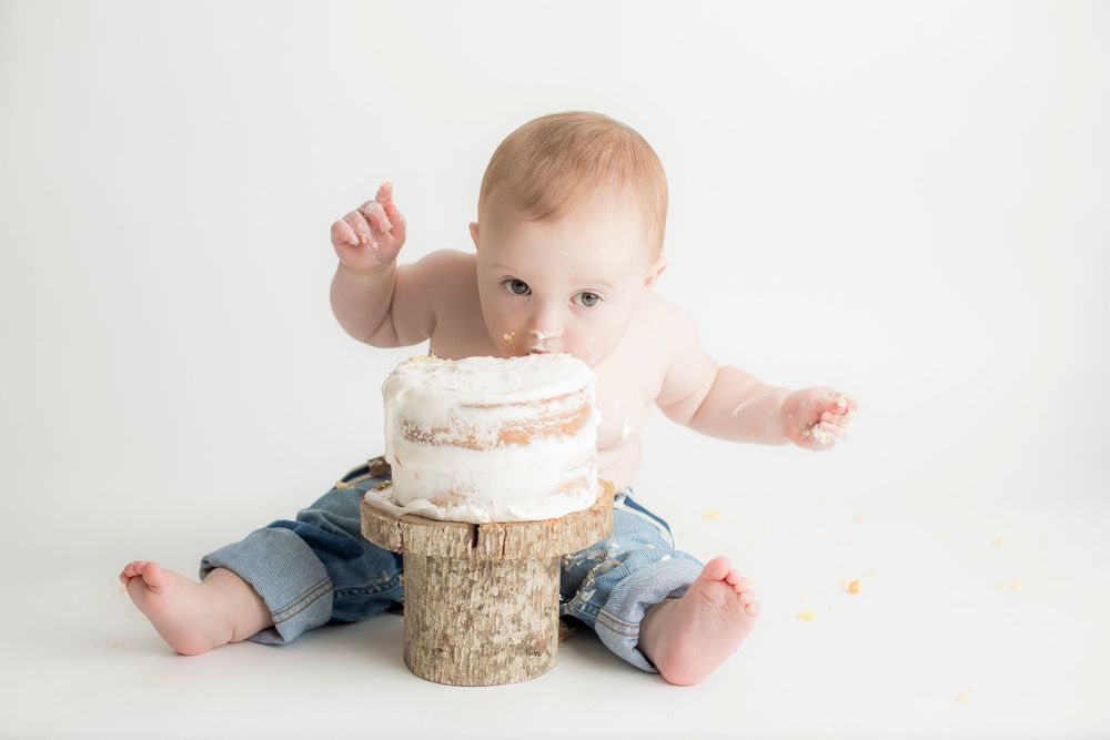 One year old baby boy eating cake with his mouth and looking at camera.