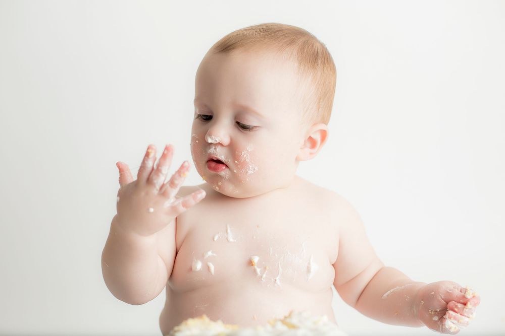 One year old baby boy looking at the icing on his fingers.