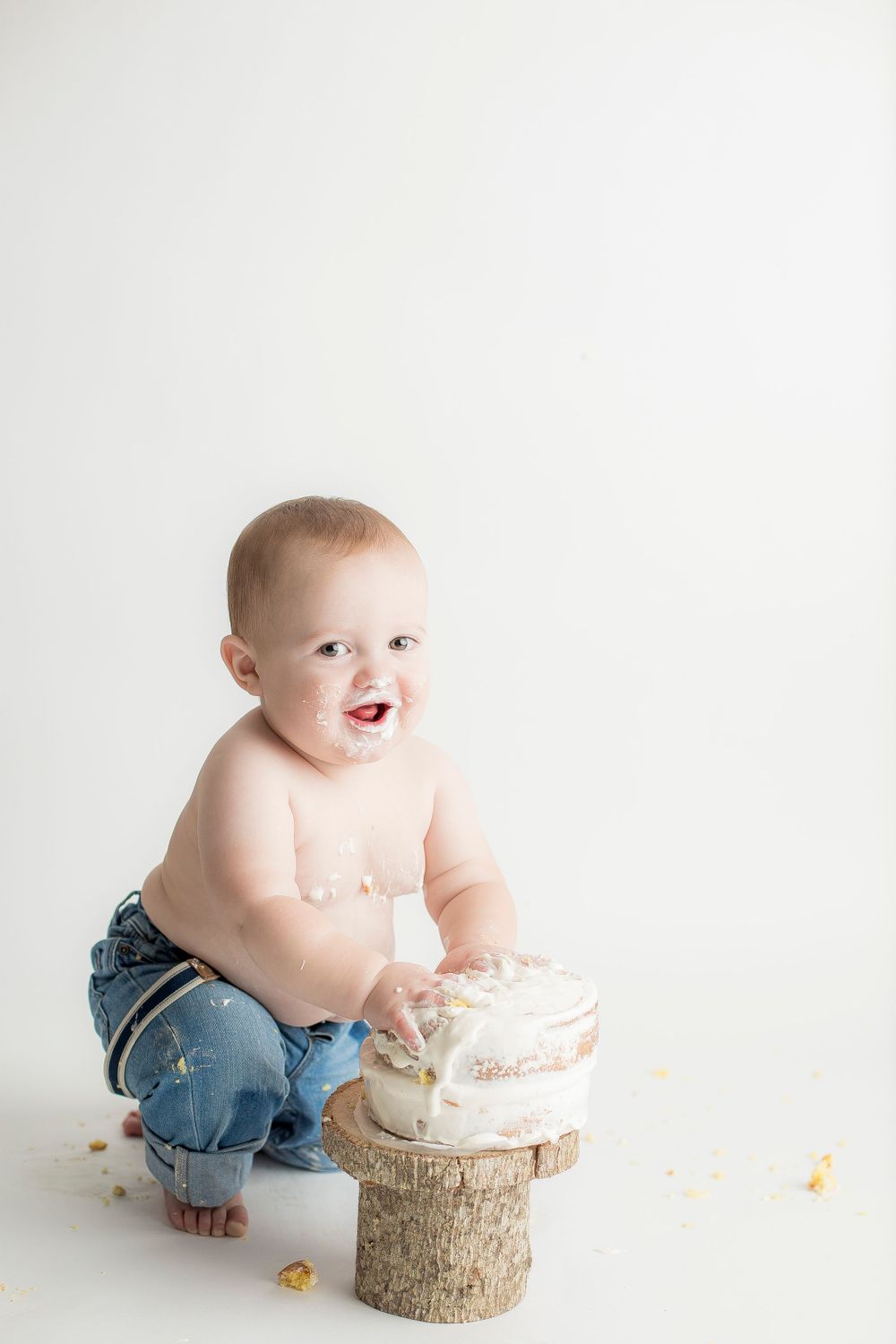 One year old baby boy squatting in front of cake smiling at the camera.