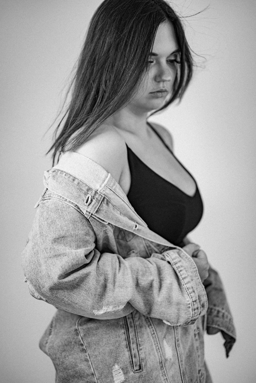 Fashion portrait of model wearing black top and denim jacket in black and white.