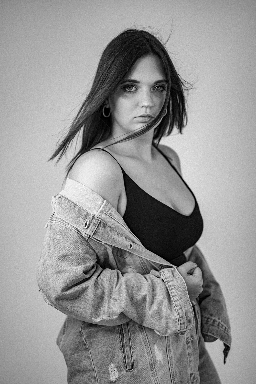Black and white portrait of model in denim jacket against neutral background.