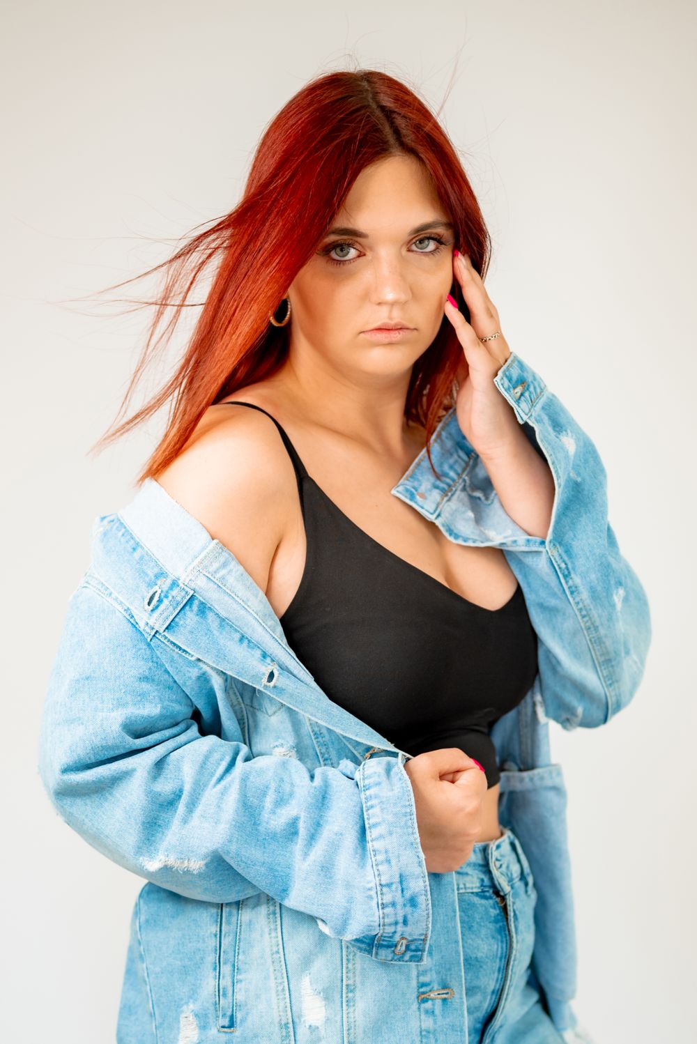 Fashion portrait with red hair, black top and oversized light blue denim jacket.
