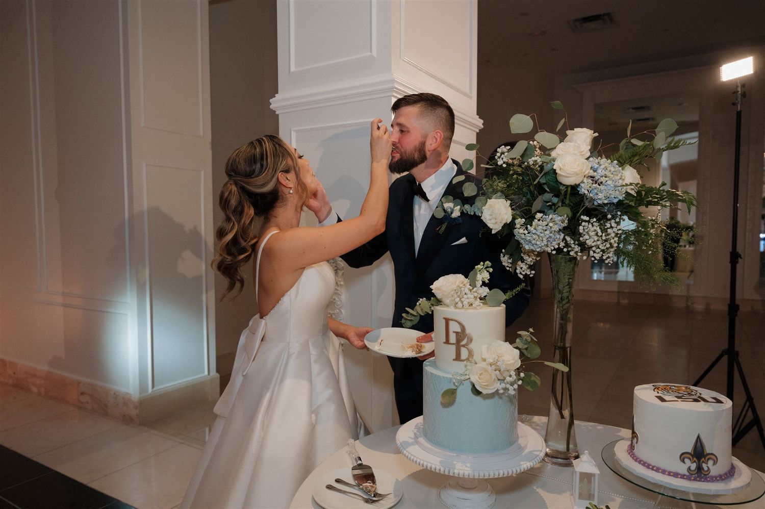 Couple sharing wedding cake together at reception with blue tiered cake and white floral arrangements on elegant display.