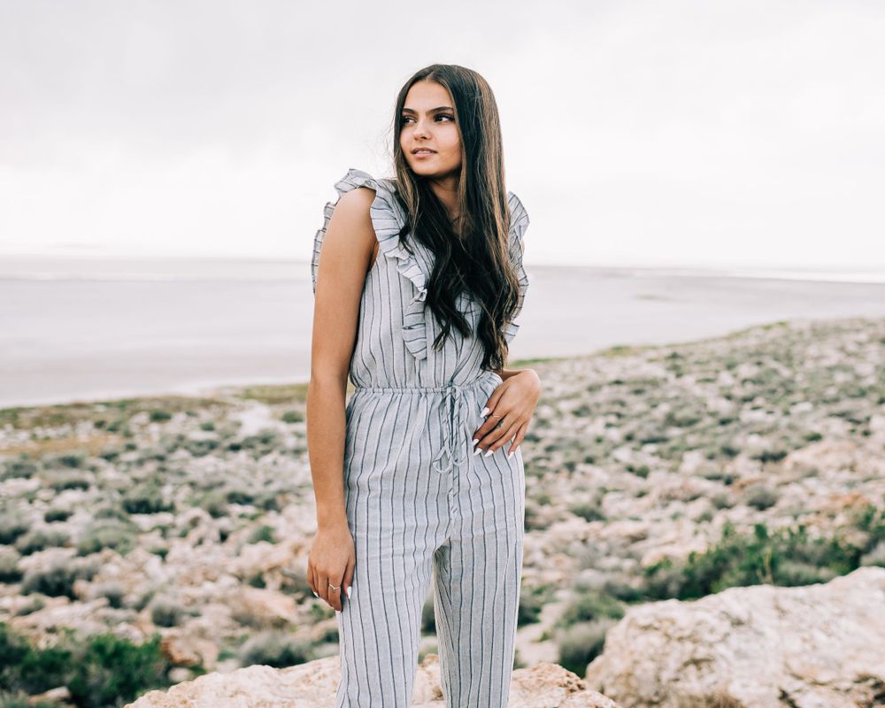 Person in striped jumpsuit stands on rocky overlook with desert landscape behind.
