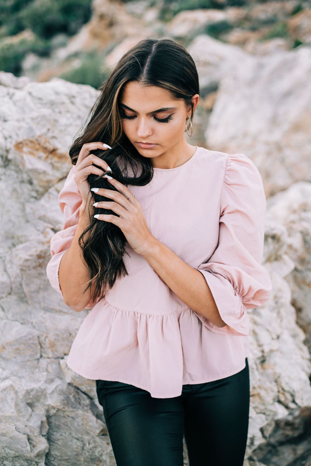 Portrait of person in pink ruffled blouse against rocky mountainous backdrop.