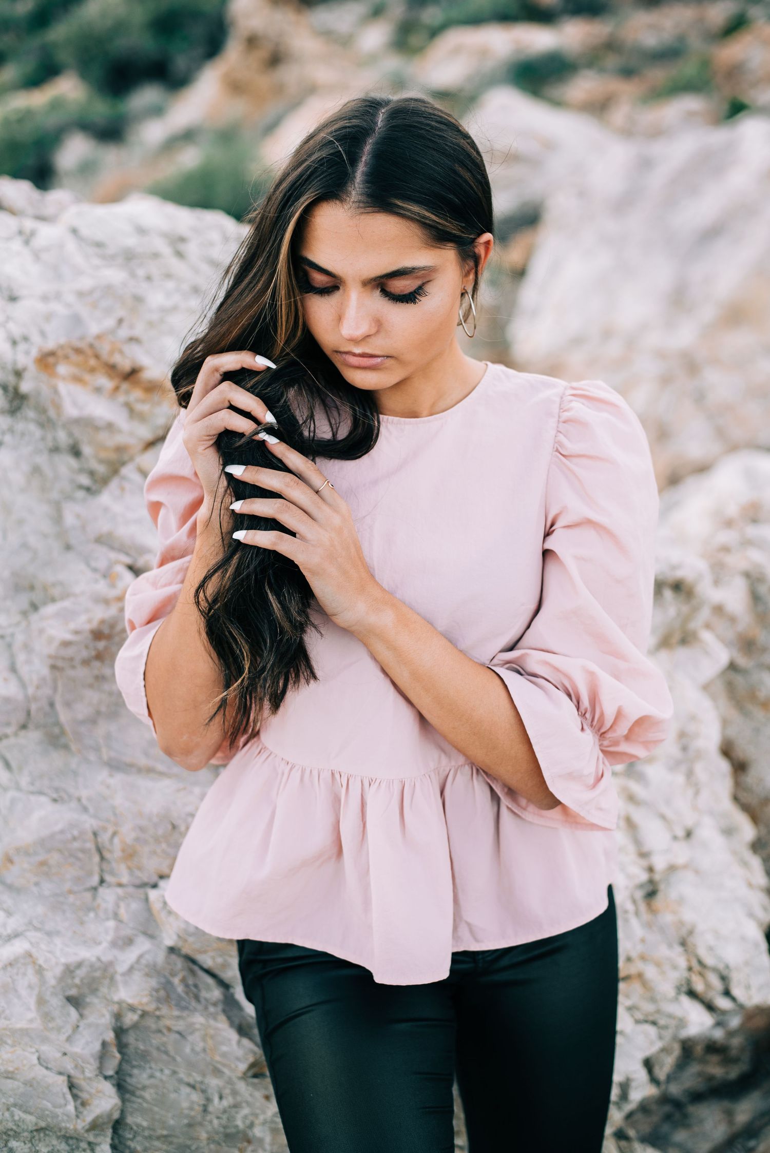Portrait of person in pink ruffled blouse against rocky mountainous backdrop.