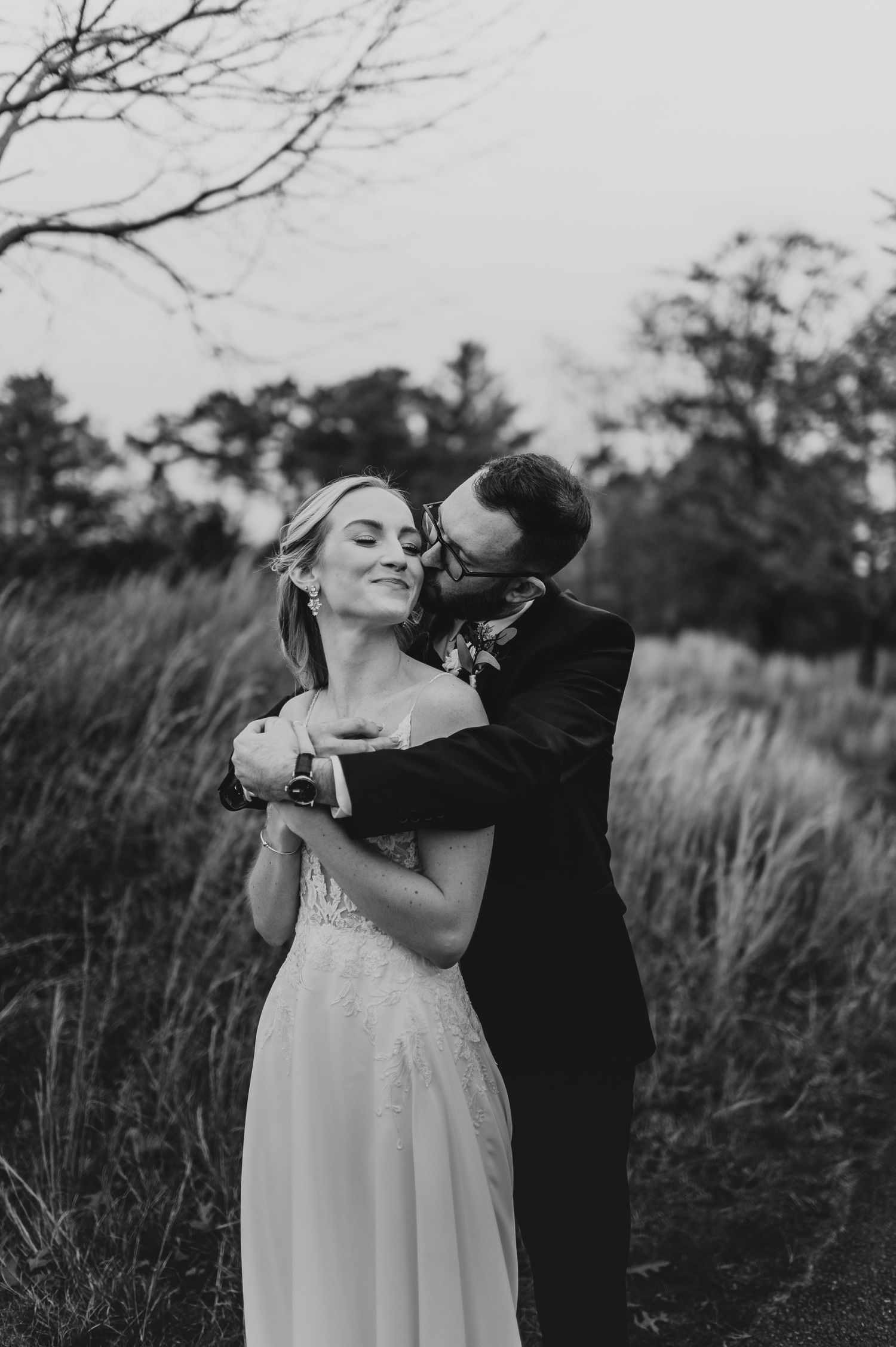 Black and white wedding portrait capturing an intimate moment in tall grass.