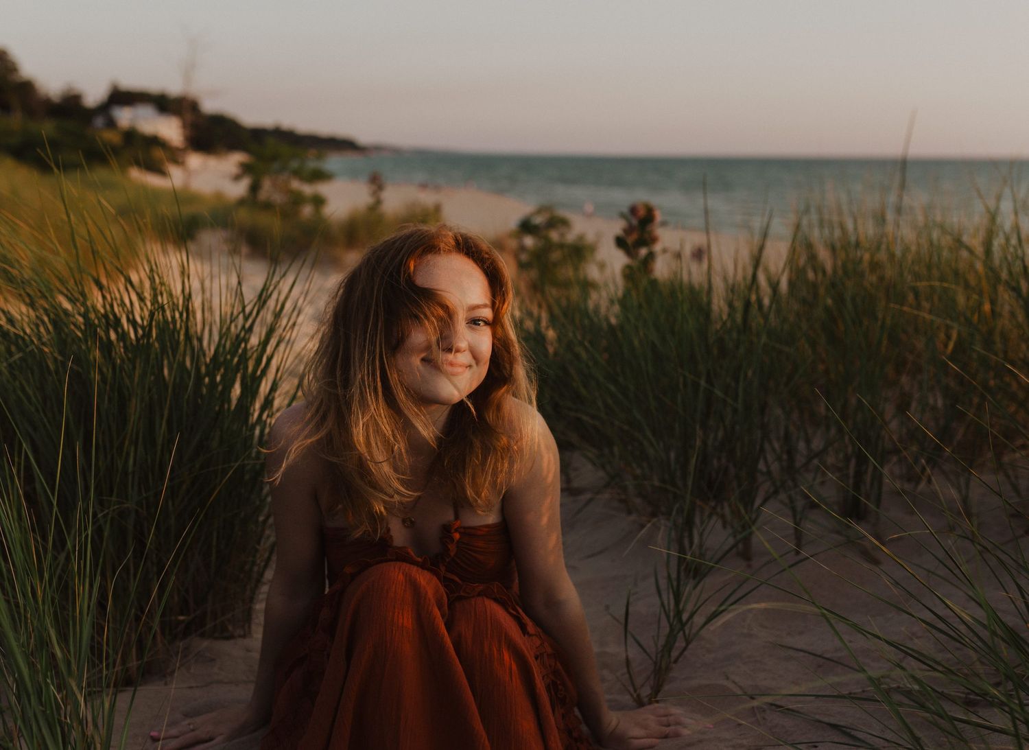 Senior in red dress sitting on grassy beach south haven Michigan