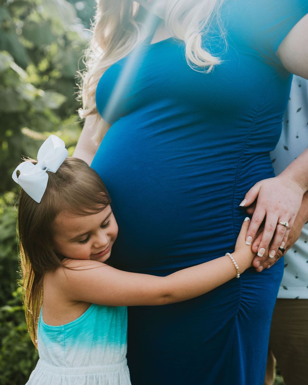 A young girl hugs her mothers very pregnant belly.