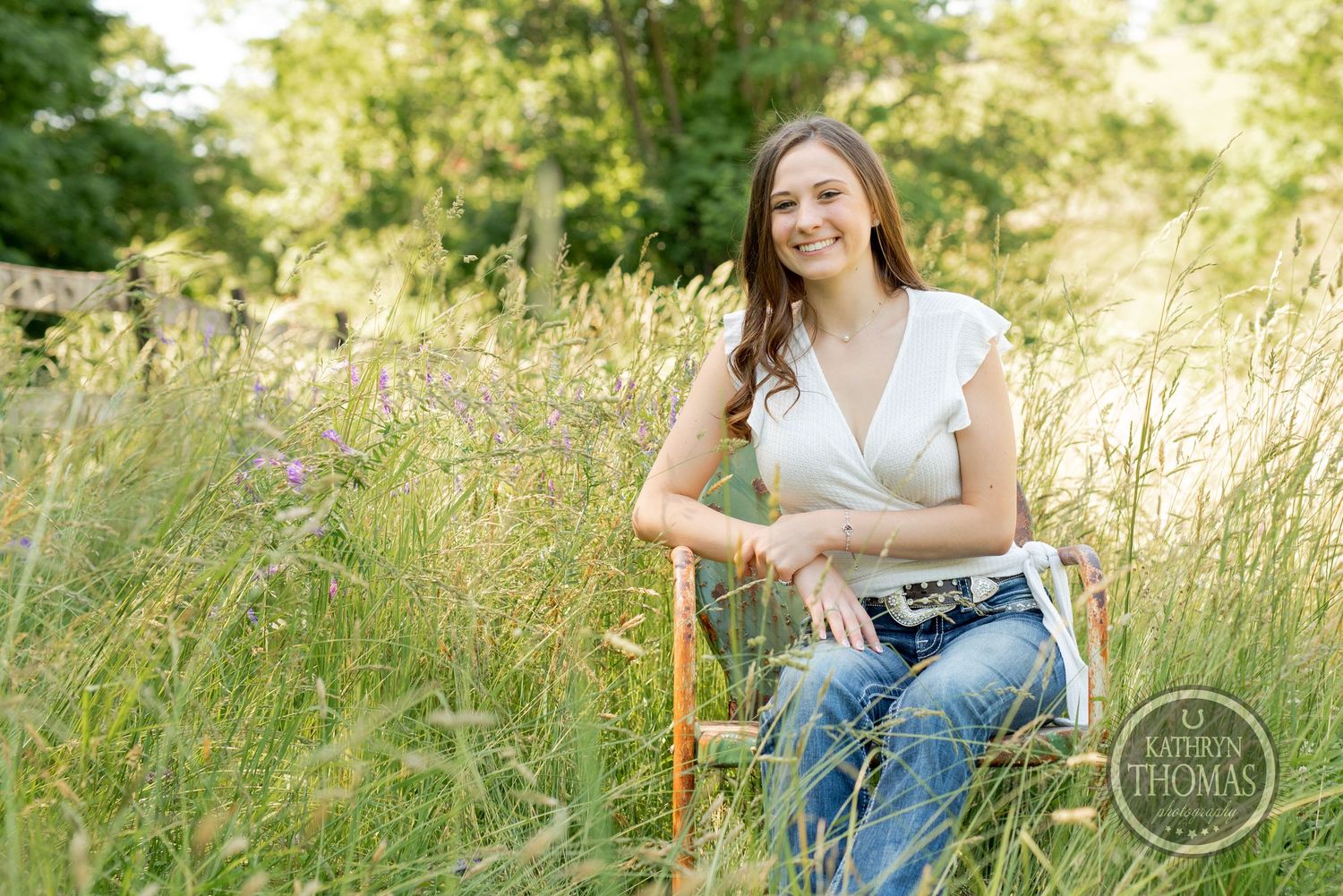 Outdoor portrait with wooden chair in meadow featuring white top and casual denim style.