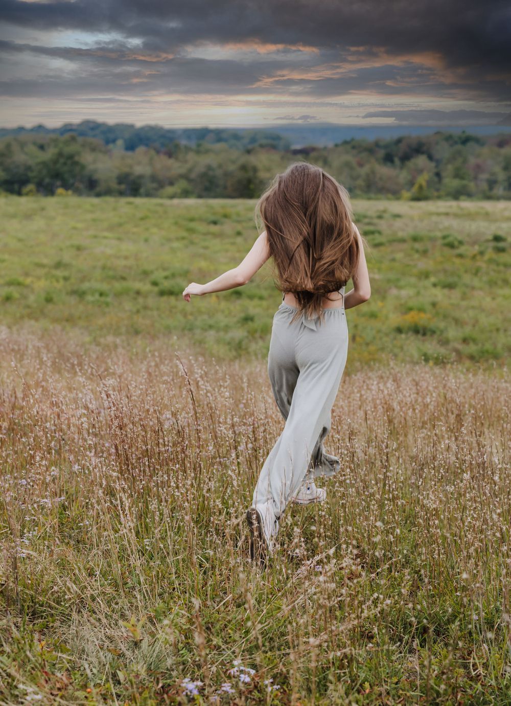 Woman in flowing dress dances through a golden meadow at sunset with windswept hair.