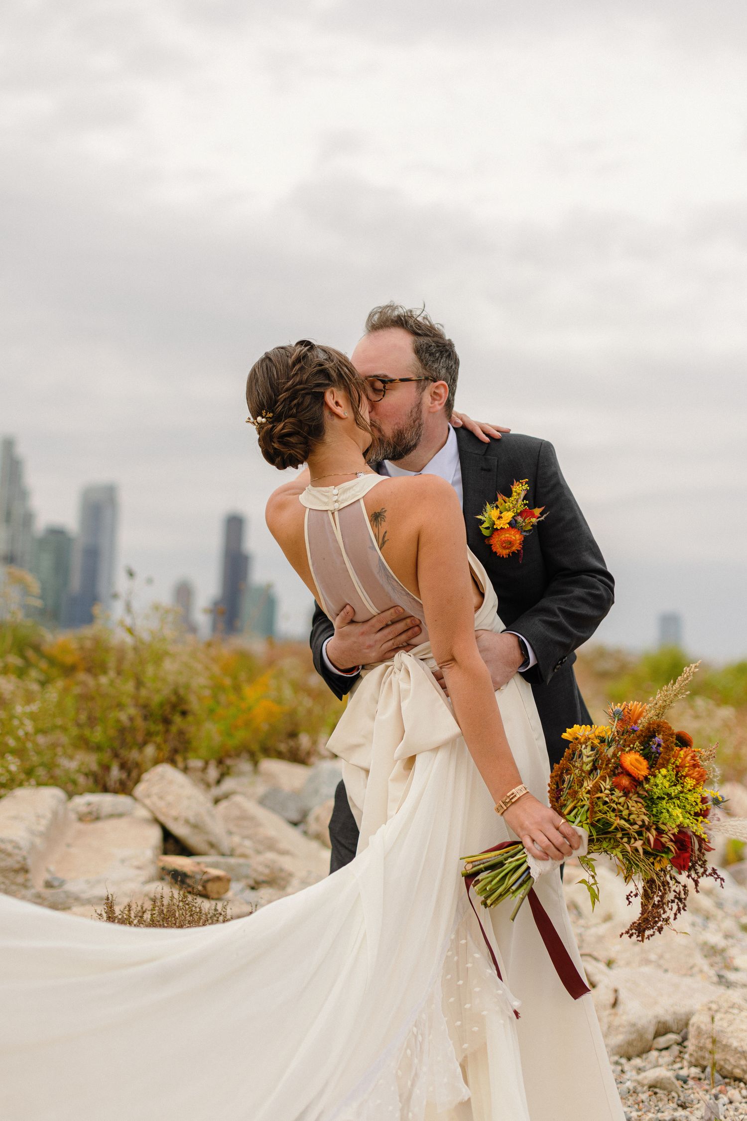 A romantic wedding kiss with a city skyline backdrop and fall florals.