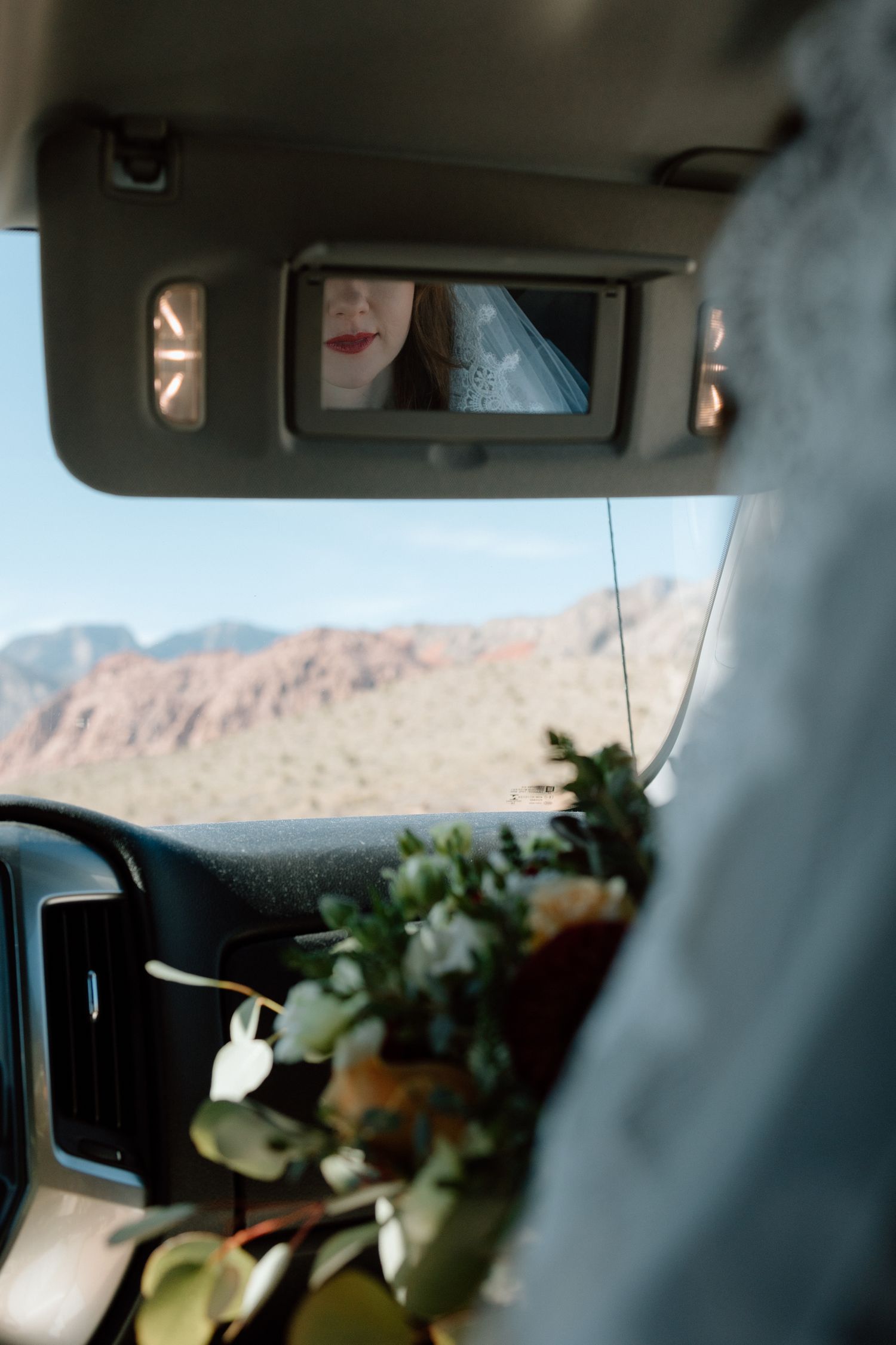 View through car visor mirror with desert mountains visible through windshield.