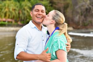 Woman kissing fiancé's cheek on the beach