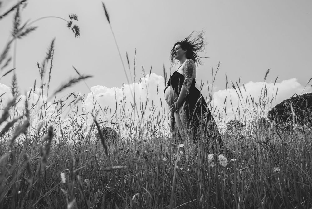 Silhouette of a figure standing in tall grass field with wind blowing their hair at sunset.