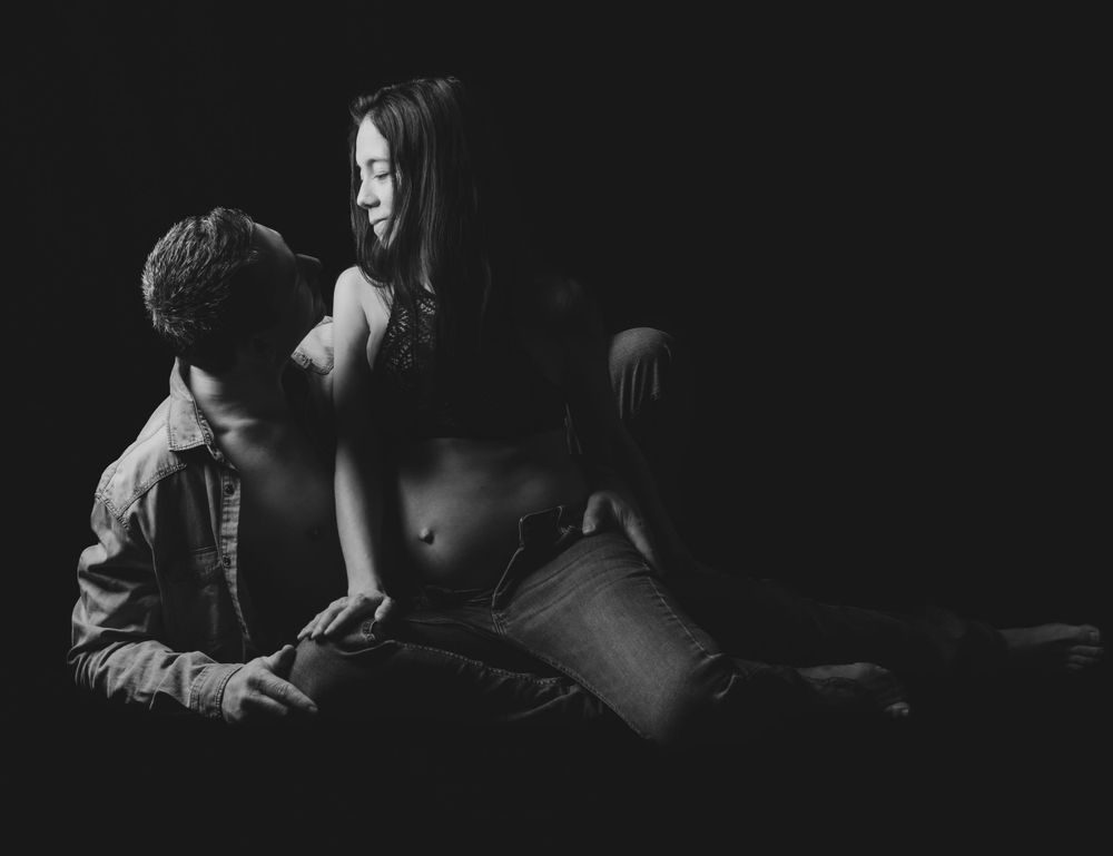 Intimate black and white portrait of couple sitting close together in dark setting.