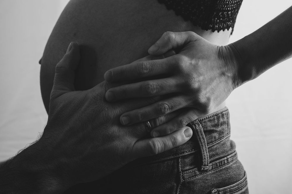 Close-up black and white photo of hands resting on a pregnant belly.